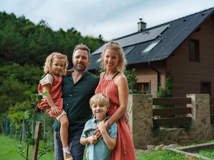 Image of family smiling for the camera with their energy efficient home with solar panels in behind